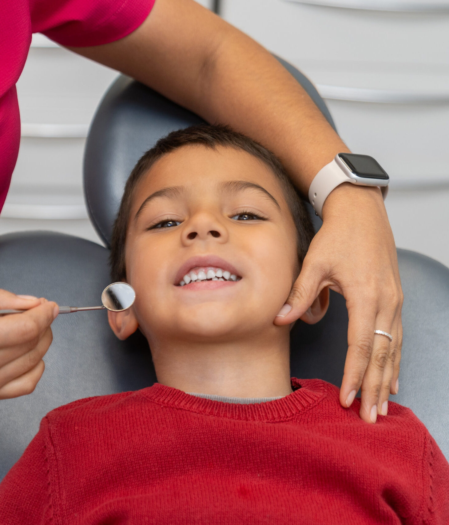 Pediatric dentist using a dental mirror to examine the teeth of a young boy during a routine checkup