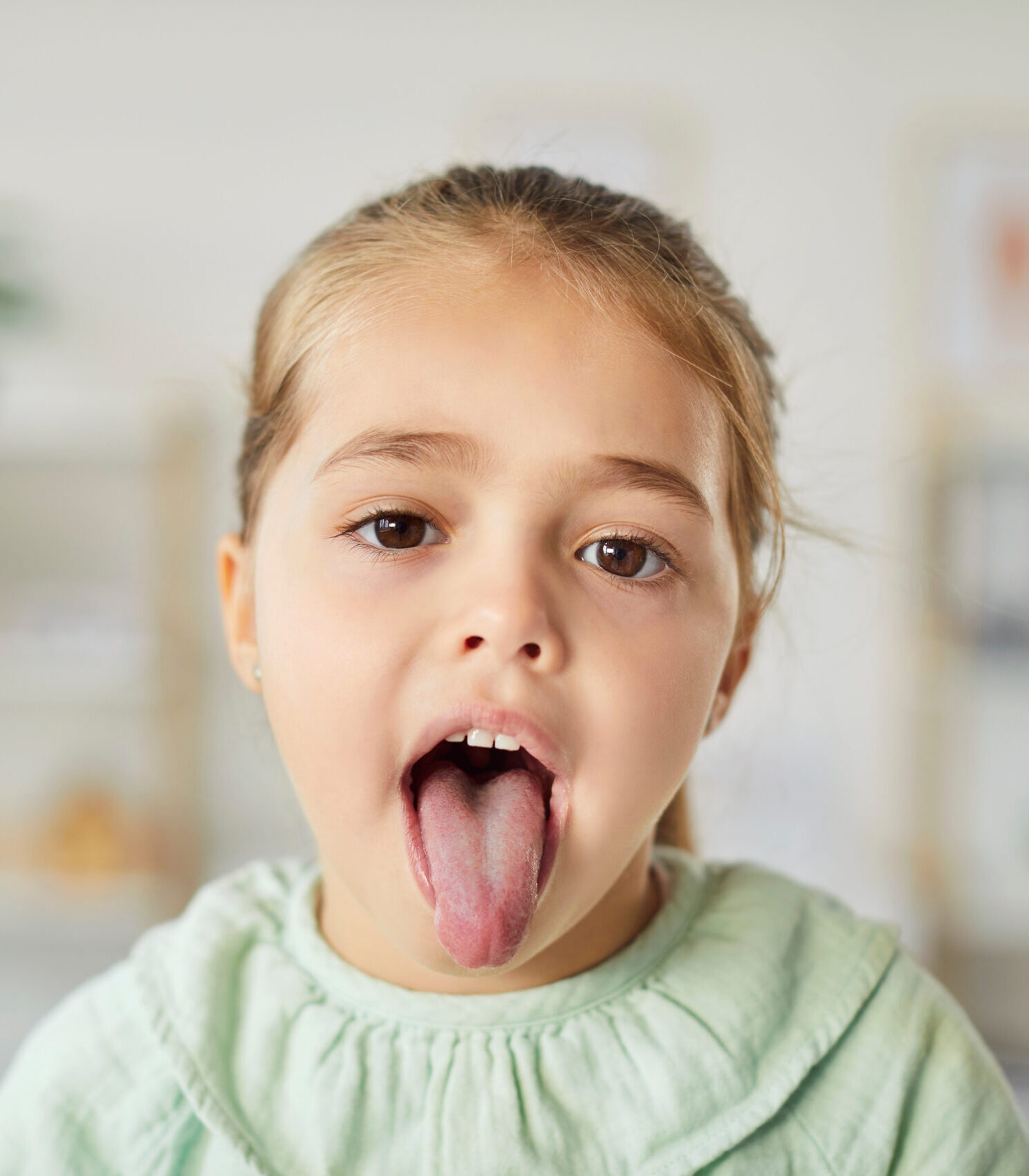 Portrait of a girl patient showing tongue for a dental or throat inspection during a healthcare checkup in a clinic. Dentistry and healthcare services focus on thorough medical examination.