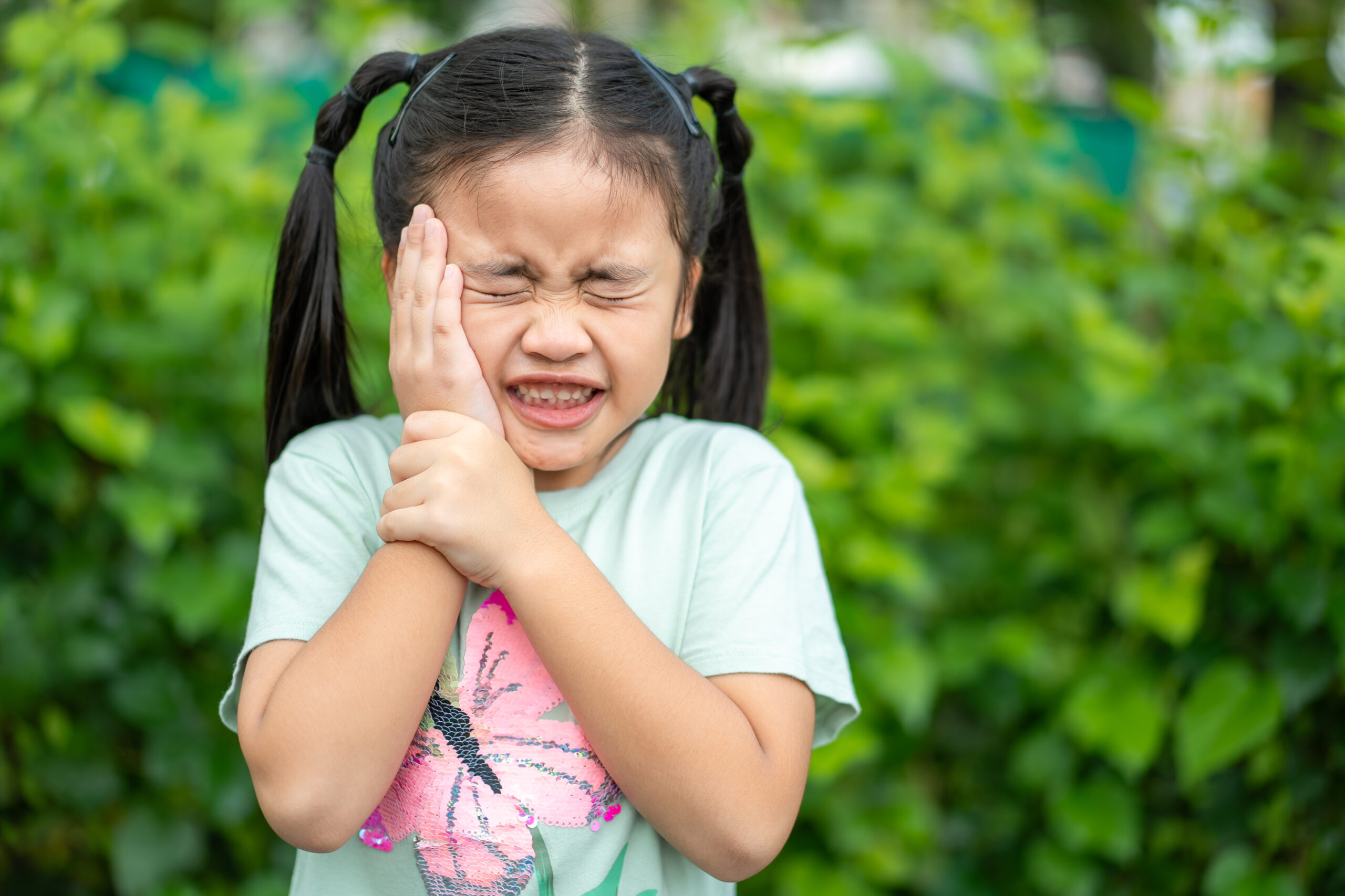 Tooth ache concept. Asian Little girl holding her cheek with hand, suffering from bad toothache. Kid with painful expression .Caries. a loose tooth, Severe tooth pain.