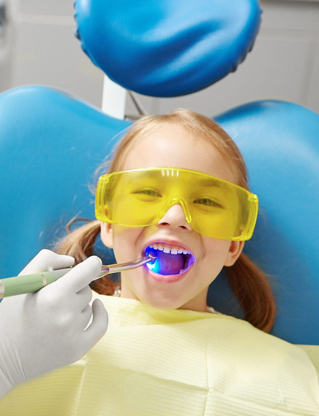 Process of drying the dental seal after treatment of the patient's tooth in pediatric dentistry. Little girl in dentist office. Doctor visiting of child.