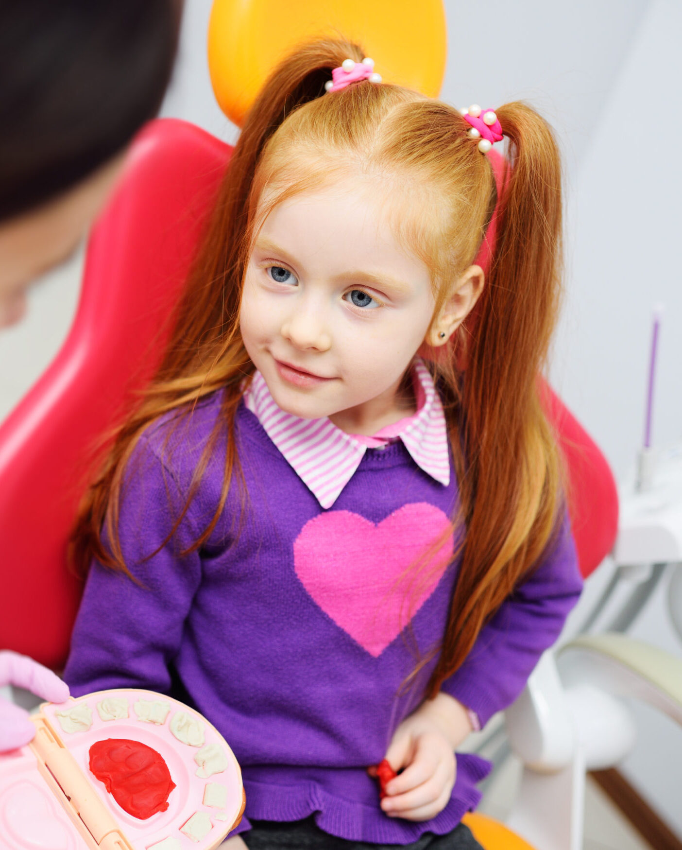 the dentist shows the little girl how to clean the teeth with a toothbrush on an artificial jaw dummy