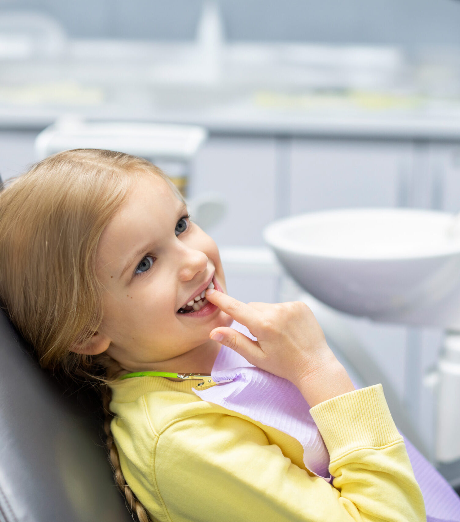 Cute little girl showing her milk teeth and waiting for checkup, sitting in chair in dentist office. Early prevention and no fear concept