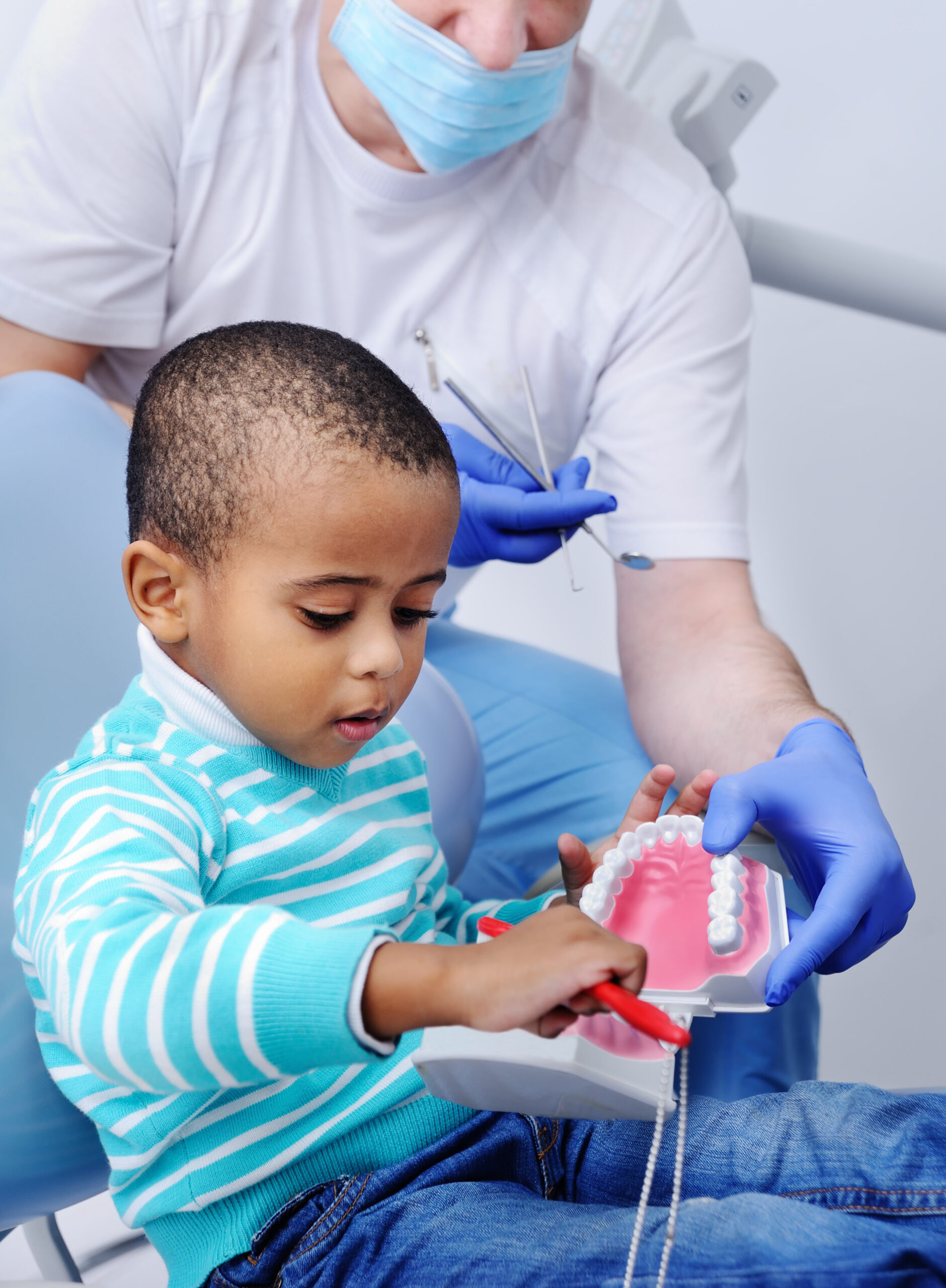 black baby boy in blue dental chair. little boy with a model of the jaw in the dental office