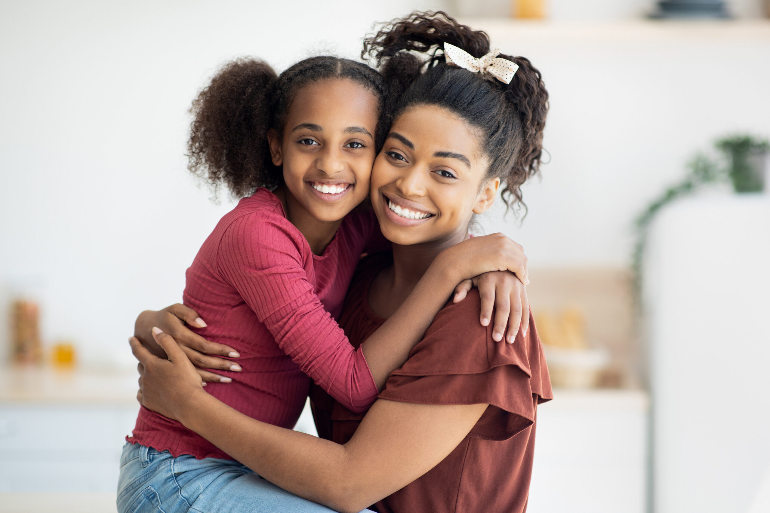 Closeup portrait of happy black mother and daughter hugging and smiling at camera, beautiful young african american woman mom and teen girl kid cuddling at kitchen, copy space