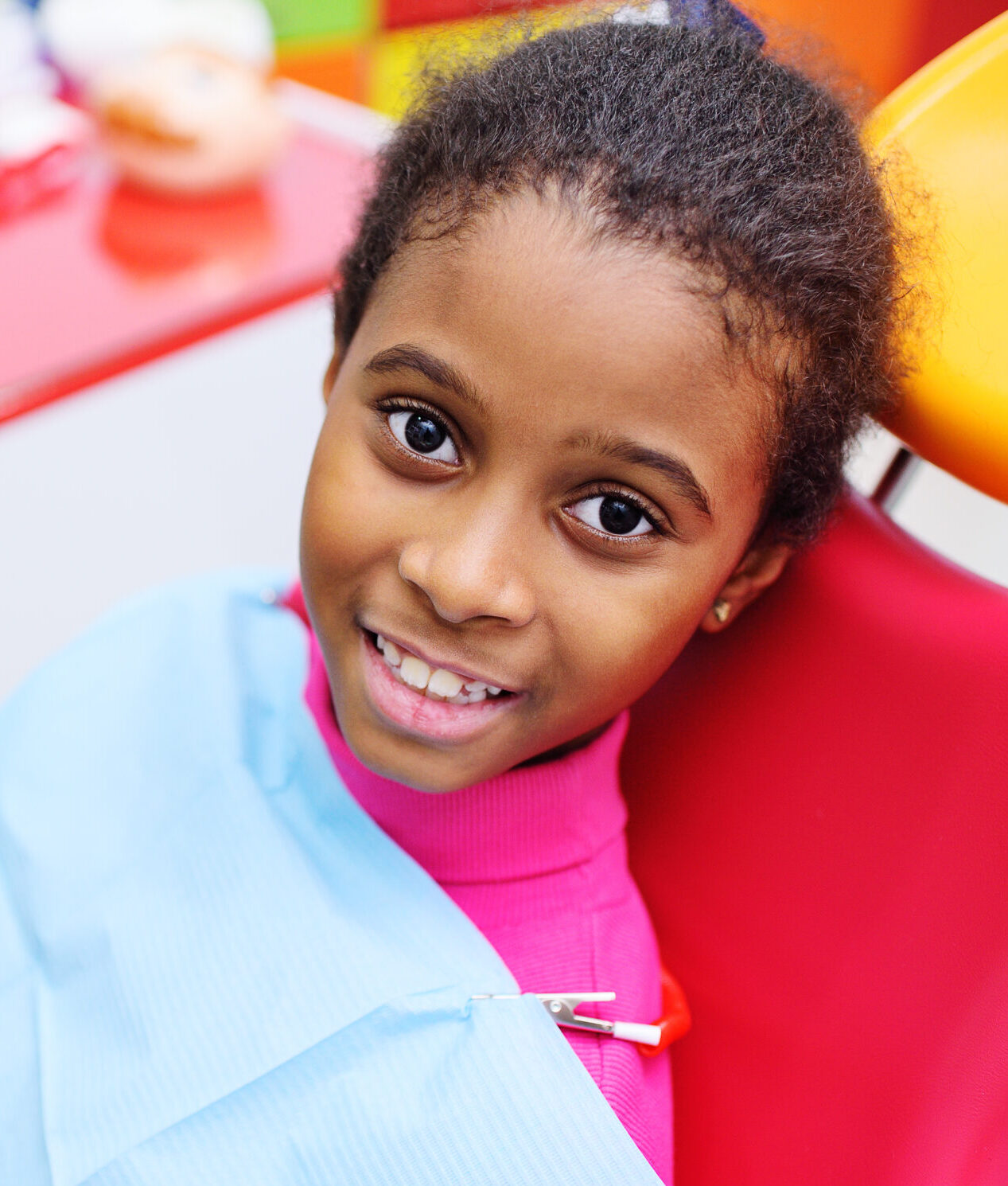 cute black baby girl smiling sitting in a red dental chair at the examination at the children's dentist