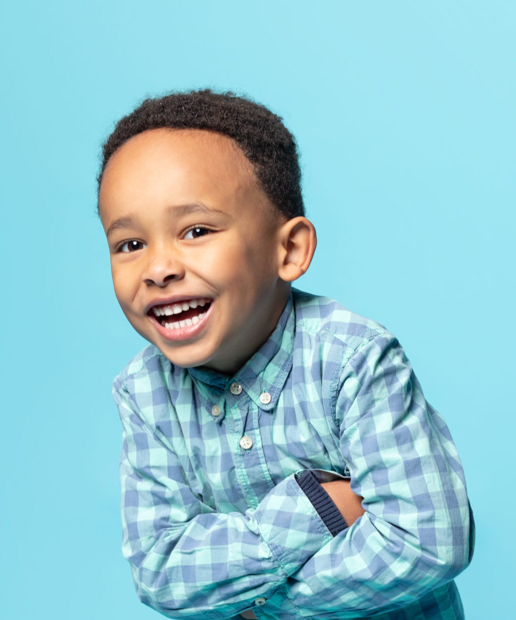 Portrait of cheerful little african american boy posing with folded arms over blue background, joyful male kid in stylish shirt smiling and looking at camera, copy space