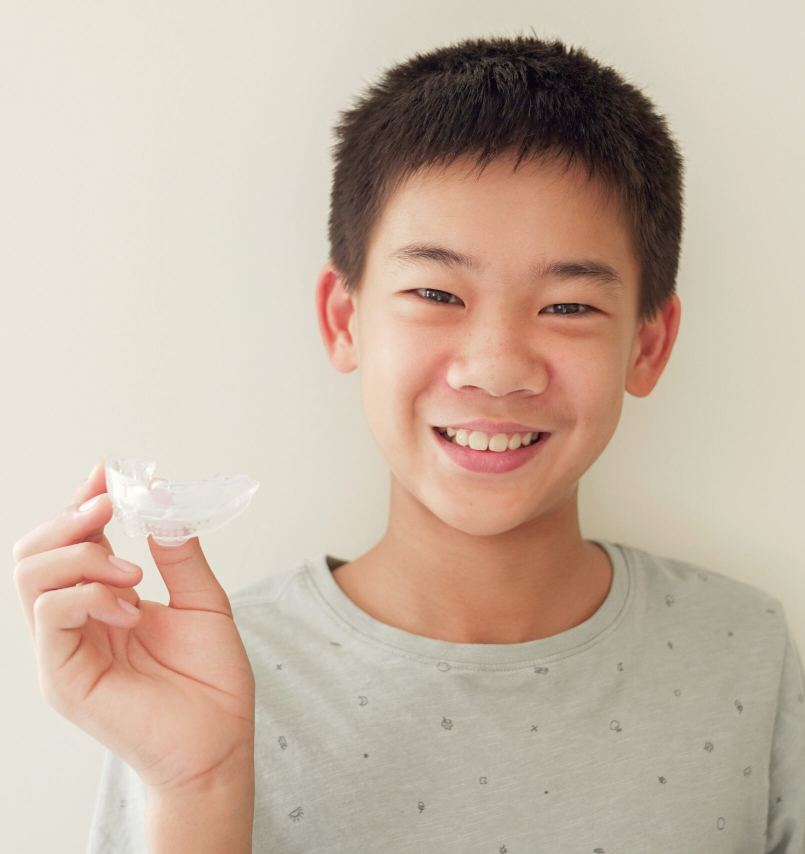 Smiling Asian preteen boy holding invisalign braces, mouthguard, teen orthodontic oral health care concept