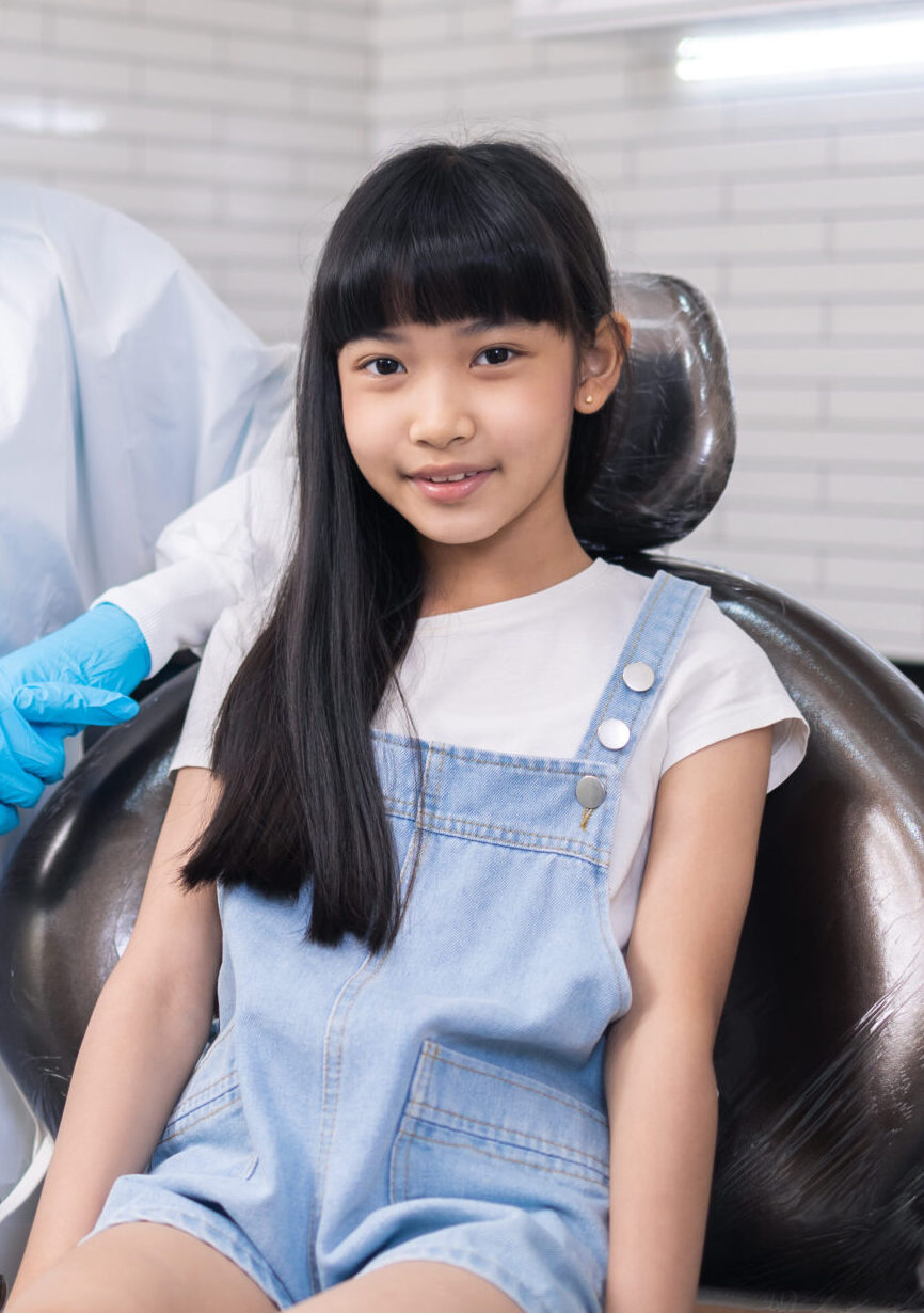 Children's dentistry for healthy teeth .Close-up happy little child asian girl smiles looking at camera, sitting in dentist's chair, receiving dental.