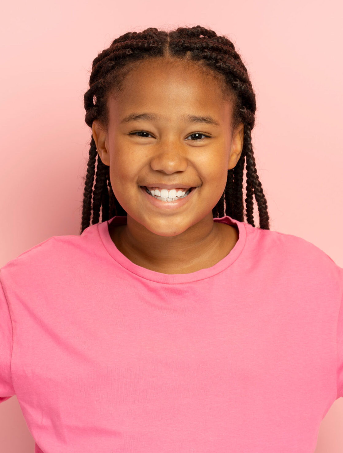 Portrait of smiling positive African American girl showing victory gesture, peace wearing stylish casual t-shirt looking at camera isolated on pink background. Attractive child posing, mockup