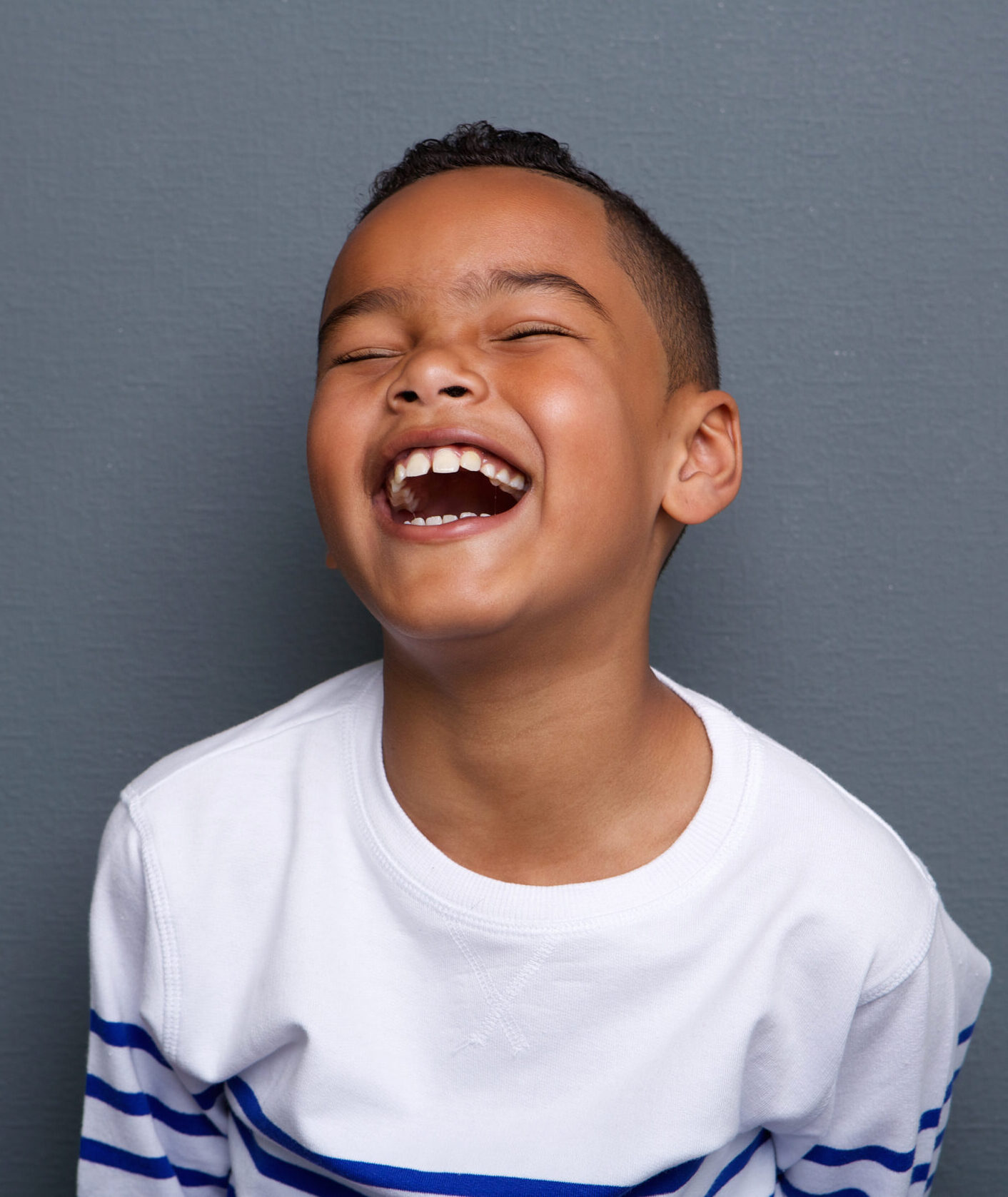 Close up portrait of an excited little boy laughing on gray background