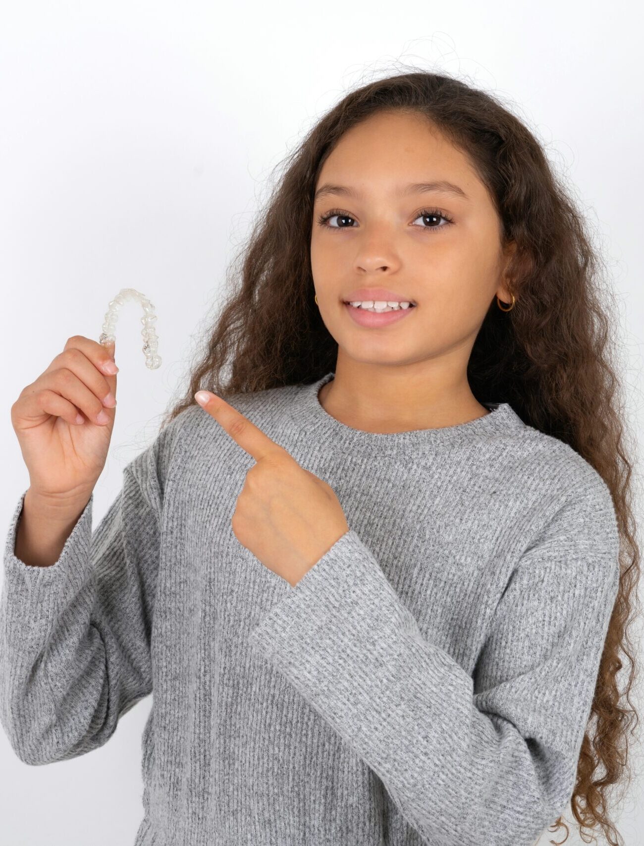 MODEL holding an invisible aligner and pointing at it. Dental healthcare and confidence concept.